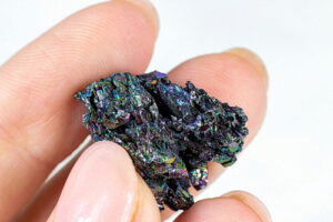 Woman hand holding shiny black Carborundum crystal (Moissanite or Silicon Carbide) on light background close up.